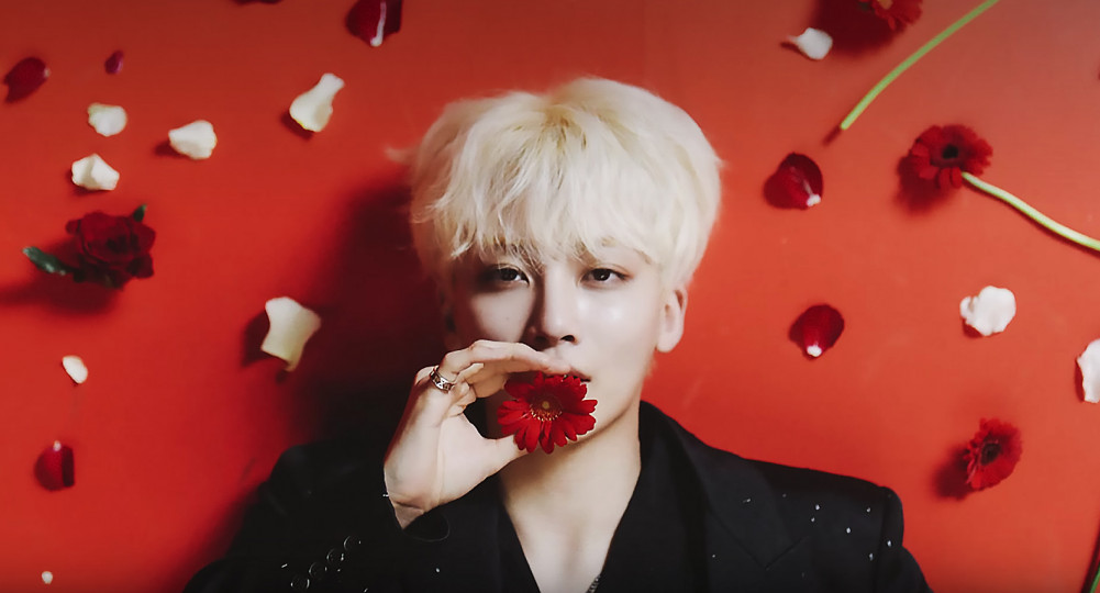 Jeonghan from Seventeen holding a red flower by his mouth.