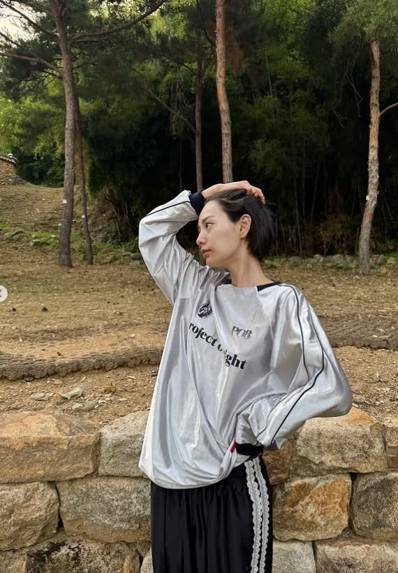 Nana mengenakan atasan putih dan rok mini gelap, berpose kasual.