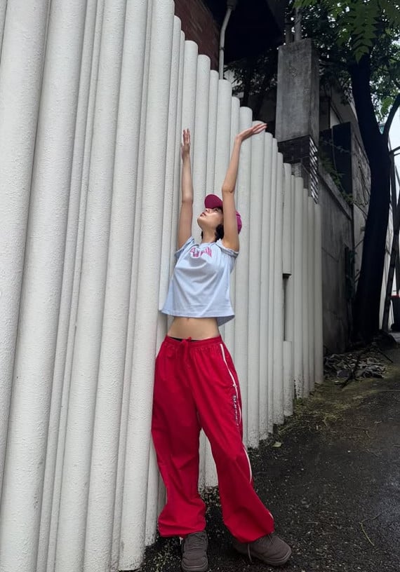 Nana berpose di tangga, mengenakan jaket ringan dan celana longgar.